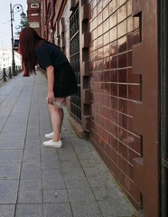 A girl with dark brown hair in a black t-shirt and a black mini skirt with a bottle of water in her hands takes photos of a city street with a smartphone on a Sunny summer day.