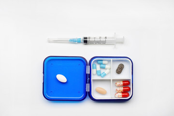 box with cells for capsules and tablets and a syringe on a white background.