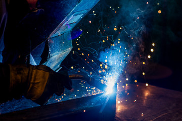 A welder in a metal factory welds metal parts, lights flash