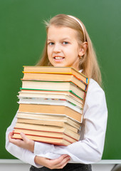 Young girl holds big pile of the books near chalkboard