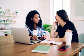 Multiracial women sincerely talking at table with laptop