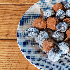 Close-up homemade date candies from bread covered with chocolate and powdered sugar on the plate on the wooden background.
