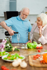 Selective focus of senior couple pouring champagne by bouquet and vegetables on kitchen table