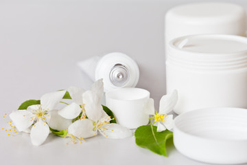 Fototapeta na wymiar Cosmetics for face and body care in white jars and tube with hand cream on a light background. Beautiful spring still life with apple tree flowers. Place for text, soft light, close-up