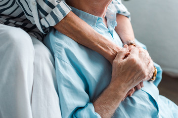 Cropped view of senior couple holding hands at home