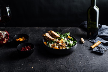 Buckwheat salad with lamb's lettuce, pomegranat seeds, goat cheese, mandarine and spring onion, Served with whole grain baguette and red wine. Black table and black background.