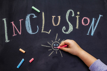 Word Inclusion on black school blackboard written with chalk. Children hand, education concept