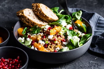  Buckwheat salad with lamb's lettuce, pomegranat seeds, goat cheese, mandarine and spring onion, Served with whole grain baguette and red wine. Black table and black background. © mateuszsiuta