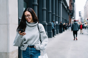 Joyful young woman texting on smartphone on street