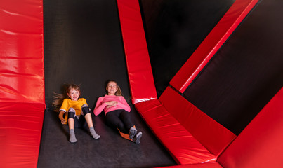 Tired happy mom ang her daughter resting after jumping on trampoline in fitness center