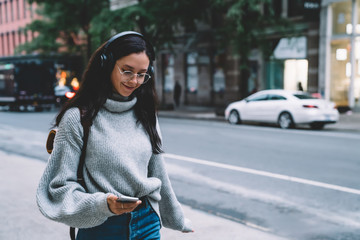 Young cheerful woman walking down street and listening to music