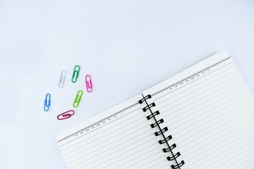 A white notebook along side some different colored paper clips on an isolated white background