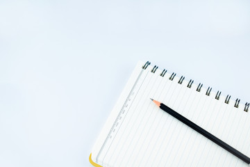 Single black wood pencil on a white notebook in an isolated white background