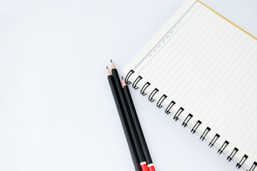 Three black wood pencils alongside a notebook in a isolated white background