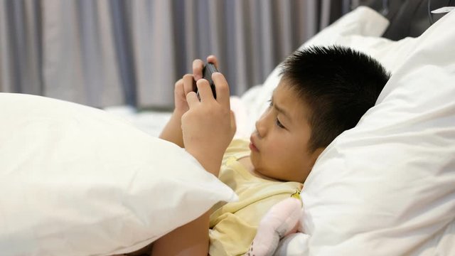 boy playing smartphone on bed, kid use phone and play game, addicted game and cartoon, 