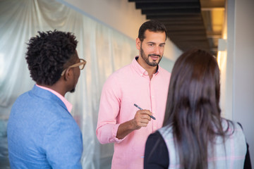 Cheerful young man talking with colleagues. Group of people communicating in corridor. Communication concept