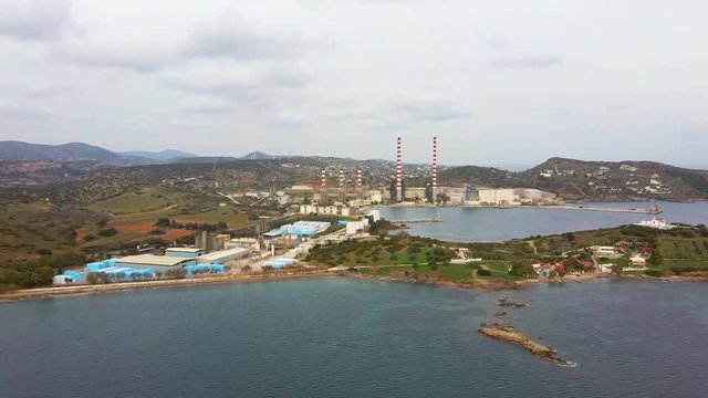 Aerial view of sea bay with old factory and a small white church, low vegetation mountains, Lavrio Greece, moving forward by drone
