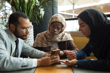 Focused people sitting at cafe and looking at smartphone. Group of young people reading information from phone. Technology, communication concept