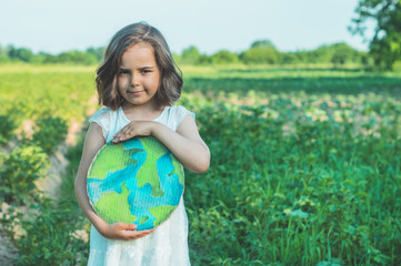 Protection and love of earth. Little girl holding planet in hands against green spring background....