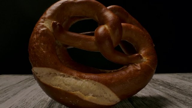 Tasty traditional knot shaped pastry named pretzel placed on lumber table in dark room.