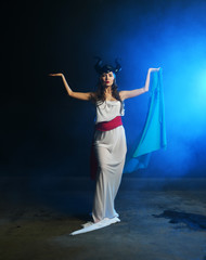 Fototapeta na wymiar beautiful girl in the clothes of the goddess of the earth with a blue veil on a background of smoke