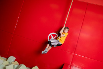 Happy child girl swinging on rope in indoor playground center