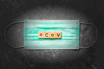 nCoV word written on wood block lying on medical mask. nCoV text on gray table for your desing, coronavirus concept top view