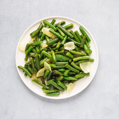 Fried wok green beans with onions and spices in a white plate on a gray background. Flat lei. Top view.