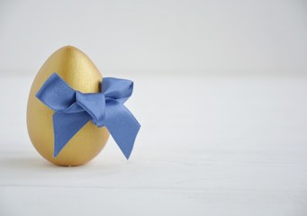 Easter.  Golden egg with a blue bow on a white background with space for text.