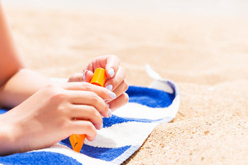 Pretty woman is lying on the towel at the beach and opening a tube of sun cream to protect her skin from sunburn
