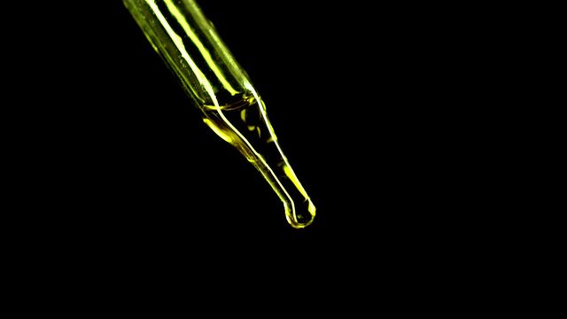 CBD oil ends with air bubbles in a dropper from a medical drop of marijuana on a black background