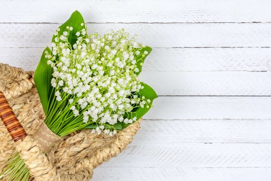 bouquet of Lily of the valley flowers in a basket on a white wooden background with a copy space close up top view
