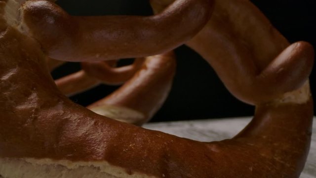 Camera zooming in to freshly baked pretzels tilting back while being arranged on timber table in dark room.