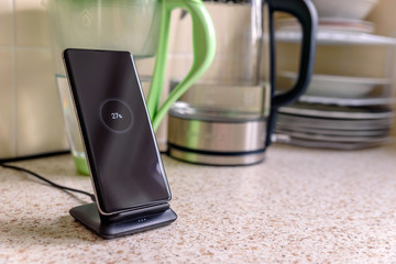 smartphone wireless charging on charging stand with 27 percent icon on screen on kitchen tabletop