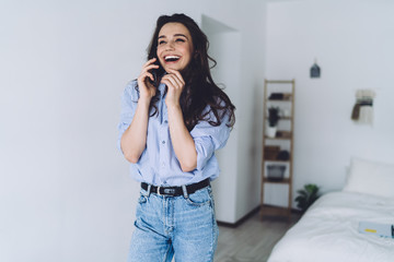 Attractive toothy smiled brunette talking on smartphone at home