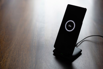 smartphone wireless charging on charging stand with 51 percent icon on screen on wooden table