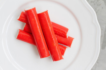 five crab sticks on a white plate, on a gray background.  Delicious crab sticks cooked for food. concept of cooking food, dish, salad. Seafood for salad. the view from the top.