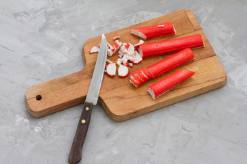 Crab stick sliced on a cutting Board, on a gray background.  Delicious crab sticks cooked for food. concept of cooking food, dish, salad. Seafood for salad. the view from the top.