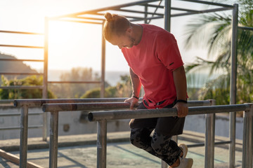 A nice young man in a red T-shirt European makes power street workout fitness outdoor, healthy...