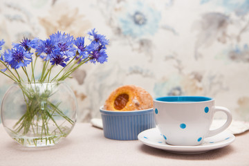 Tea in cup with dots, sweets food and vase of cornflower flowers, tender still life