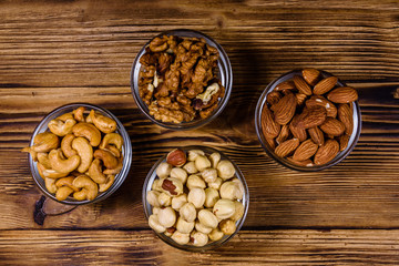 Various nuts (almond, cashew, hazelnut, walnut) in glass bowls on a wooden table. Vegetarian meal. Healthy eating concept. Top view