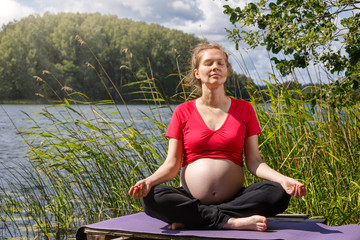 Fototapeta na wymiar Pregnant woman doing yoga exercise meditating in a summer forest