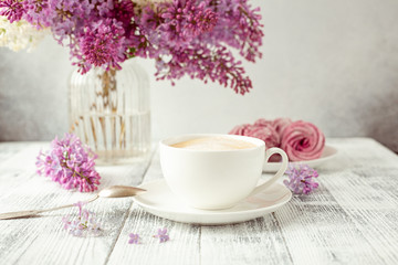 Cup of coffee, homemade marshmallow, lilac flowers. Romantic spring morning Selective focus
