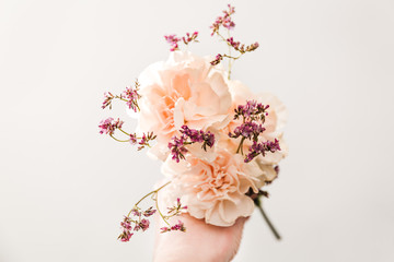 bouquet of flowers in the hand on the tint blue background, symbol of love, pink or beije carnations and small branch