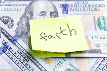 Yellow stick note on an USD money background. The inscription "faith" on a yellow memory sticky note. Close up