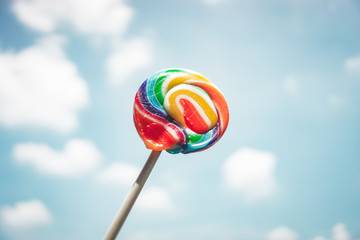 Colorful rainbow lollipop swirl with blue sky and cloud background
