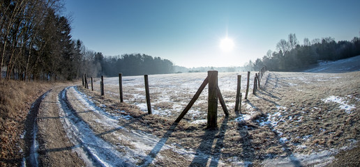 A cold winter landscape with snow and sunshine in Germany. A path leads between a forest and a pasture.