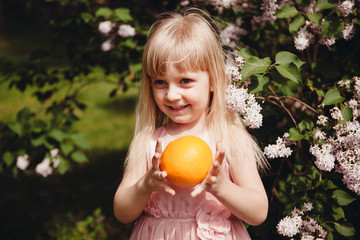 Cute little girl smile with orange fruit in hands outdoors, healthy organic food	