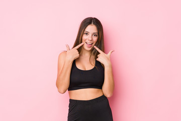 Young fitness caucasian woman isolated smiles, pointing fingers at mouth.