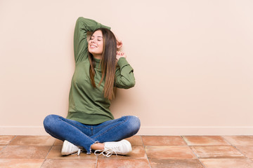 Young caucasian woman sitting on the floor isolated stretching arms, relaxed position.